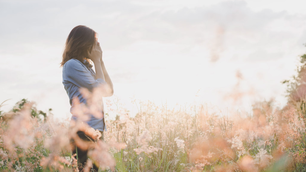 Sad woman standing in field with sunset background.